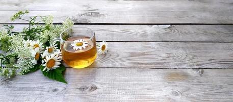 chá de camomila e um buquê de camomilas. copo de vidro com chá em tábuas de madeira. foto
