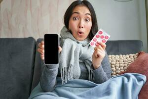 conectados médicos e assistência médica. sorridente coreano mulher mostra Móvel telefone tela e medicamento, pegando frio, ficando às casa e recomendando Smartphone gp foto