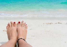 pés de mulher e unhas vermelhas na praia foto