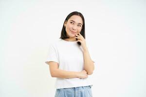 retrato do ásia mulher pensamento, olhando acima com pensativo face, em pé dentro camiseta sobre branco fundo foto