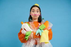 engraçado menina segurando grande quantidade do reciclando lixo, plástico desperdício para reciclar, azul fundo foto