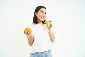 retrato do lindo jovem mulher com saudável em forma dieta, bebidas suco a partir de fresco espremido laranja fruta, branco fundo foto