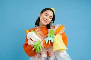 retrato do sorridente ásia mulher abraçando esvaziar plástico garrafas e reciclável lixo, eco-ativista curtidas para reciclar, azul fundo foto