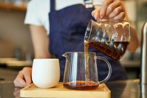 fechar acima do vidro jarra e uma copo em pé em cafeteria contador, barista derramando filtro café e preparando ordem foto