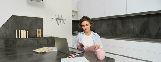 retrato do jovem lindo mulher, estudos às lar, vira dela pasta de trabalho, trabalho a partir de lar, usa computador portátil para aprender em controlo remoto, faz notas durante webinar foto