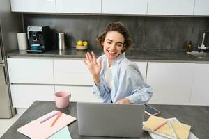 feliz jovem mulher, tutor professor alunos on-line. menina conecta para controlo remoto trabalhos encontro a partir de dela casa computador portátil, diz olá, ondas mão às computador foto