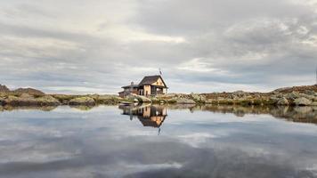 pequena cabana alpina espelhada em lago de montanha foto