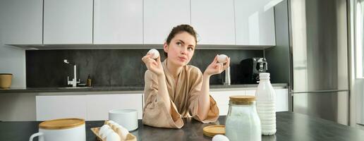 atraente jovem alegre menina cozimento às a cozinha, fazer massa, segurando receita livro, tendo Ideias foto