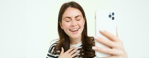 retrato do mulher rindo enquanto levando selfie com engraçado foto filtros, em pé sobre branco isolado fundo