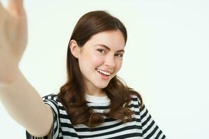 retrato do lindo jovem mulher, 25 anos velho, detém Smartphone, leva selfie, posando para uma foto, em pé sobre branco fundo foto