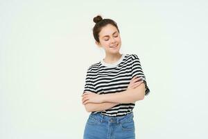 retrato do atraente, à moda jovem mulher, 25 anos velho, vestindo camiseta, Cruz braços contra peito e sorridente, olhando confiante, isolado sobre branco fundo foto