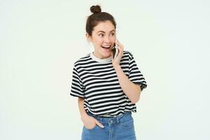 retrato do entusiasmado jovem mulher falando em Móvel telefone, conversando com amigo, reage para surpreendente notícia recebido de Telefone, branco fundo foto