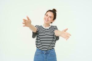 retrato do sorridente jovem mulher alcançando dela mãos, abraçando você, quer para abraçar, alongamento braços para receber, levar smth, em pé sobre branco fundo foto