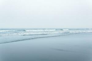nebuloso paisagem marítima, frio oceano costa com uma Largo de praia foto