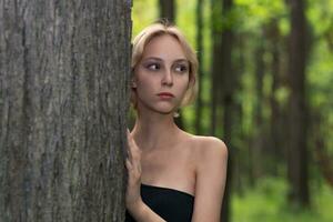 lindo menina Próximo para a árvore em uma borrado floresta fundo foto