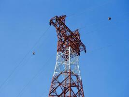 Alto Voltagem poder linhas torre em verde montanha, vermelho Alto pilone alta voltagem poder linhas, Alto Voltagem elétrico transmissão torre para produzindo eletricidade às Alto Voltagem eletricidade postes foto