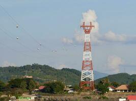 Alto Voltagem poder linhas torre em verde montanha, vermelho Alto pilone alta voltagem poder linhas, Alto Voltagem elétrico transmissão torre para produzindo eletricidade às Alto Voltagem eletricidade postes foto