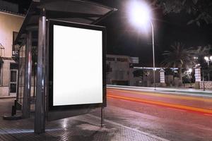 Anúncio de abrigo de ônibus em branco com semáforos desfocados à noite foto