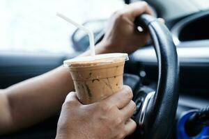 motorista de mulher asiática segura xícara de café gelado e pão de sanduíche para comer e beber no carro, perigoso e corre o risco de um acidente. foto