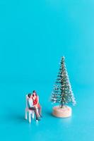 pessoas em miniatura, casal apaixonado sentado ao lado de uma árvore de natal foto