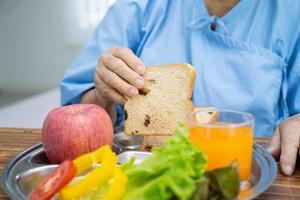 paciente asiático sênior ou idosa idosa comendo alimentos saudáveis de vegetais de café da manhã com esperança e feliz enquanto está sentado e com fome na cama no hospital. foto