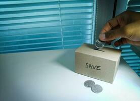 salvando dinheiro com mão colocando moedas dentro uma caixa poupança foto