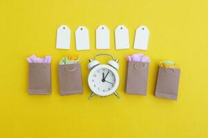 em branco etiquetas com papel bolsas, a vintage branco relógio em uma brilhante amarelo fundo. foto