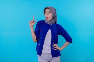 jovem carismática bonita com hijab apontando isolado em fundo azul claro