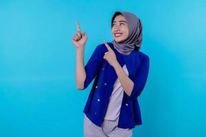 jovem carismática bonita com hijab apontando isolado em fundo azul claro
