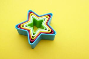 plástico Bolores do multi cores para fazer biscoitos dentro a forma do uma Estrela em uma amarelo fundo. foto