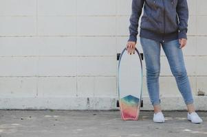 mulher asiática com surfskate contra parede de concreto foto