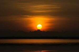 nascer do sol em laranja céu e Sombrio nuvem às a lago. foto