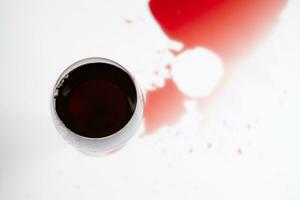 vermelho vinho dentro uma transparente vidro e derramado beber em uma branco fundo foto