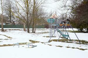 crianças Parque infantil dentro inverno debaixo neve. balanço, carrossel e deslizar. inverno desolação foto