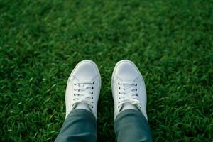 ai gerado moda estilo de vida pés dentro branco tênis em exuberante verde Relva foto