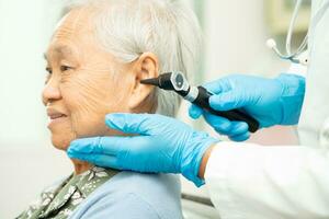 audiologista ou ent médico usar otoscópio verificação orelha do ásia Senior mulher paciente tratando audição perda problema. foto