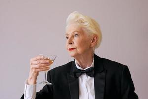 elegante sommelier maduro mulher sênior de smoking com uma taça de vinho espumante. diversão, festa, estilo, estilo de vida, álcool, conceito de celebração foto