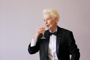 elegante sommelier maduro mulher sênior de smoking com uma taça de vinho espumante. diversão, festa, estilo, estilo de vida, álcool, conceito de celebração foto