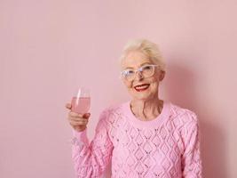 feliz mulher sênior caucasiana em cashmere rosa suéter bebendo rosa sobre fundo rosa. celebrando, amor, aposentadoria, conceito maduro foto