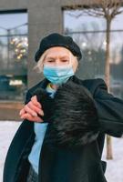 mulher elegante sênior na boina e elegante casaco preto e máscara médica, caminhar ao ar livre. bloqueio, pandemia, conceito de proteção