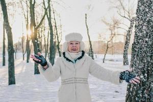 mulher sênior com chapéu branco e casaco, aproveitando o inverno no parque de neve. inverno, idade, conceito de estação