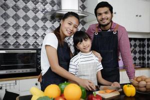 família feliz tem pai, mãe e sua filha cozinhando juntos na cozinha foto