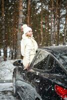 jovem mulher dentro de lã branco chapéu ter uma Diversão dentro carro. inverno viagem, coberto de neve árvores dentro a floresta. Nevado clima. Alto qualidade foto