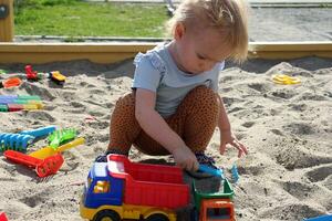 pequeno menina tocam dentro a caixa de areia com brinquedos. foto