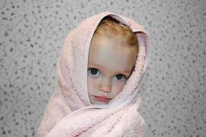 uma pequeno menina é embrulhado dentro uma toalha depois de tomando banho. fechar-se retrato. foto