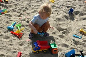 pequeno menina tocam dentro a caixa de areia com brinquedos. foto