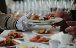 a garçom coloca aperitivos em a do homem prato durante a bufê mesa foto