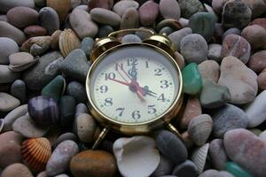 velho cobre alarme relógio em suave colori pedrinhas e conchas do mar foto