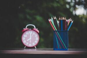 despertador e giz de cera colorido na mesa de madeira com bokeh foto