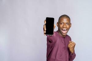 sorridente jovem africano americano homem cara africano roupas, posando isolado em branco parede fundo. aguarde Móvel telefone com em branco esvaziar tela pessoas estilo de vida conceito. foto